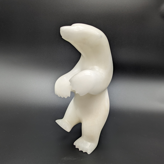 A dancing bear carved from white alabaster. The bear dances on one foot, with the other hind foot raised and its paws in front of it. This bear faces left.