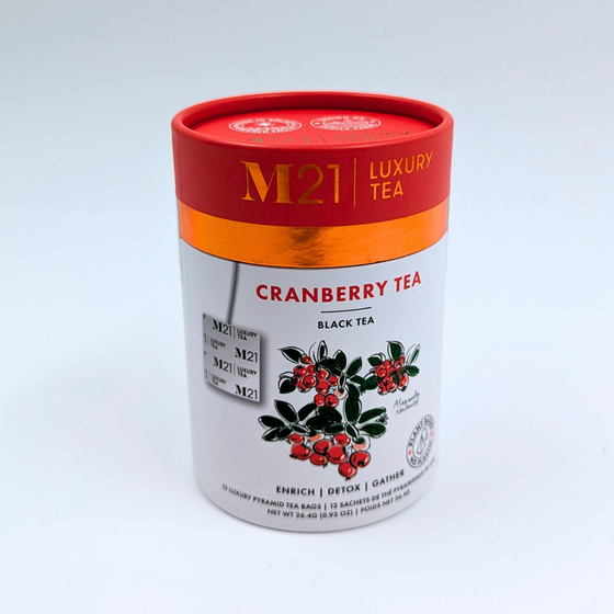 A cylindrical box that holds twelve cranberry flavoured tea bags. The tea bags are pyramid shaped and are blended and packed in Canada. The container is made from 100% recycled paper. The illustration on the box depicts red cranberries and matches the red coloured lid. It includes instructions to brew for three to five minutes. 