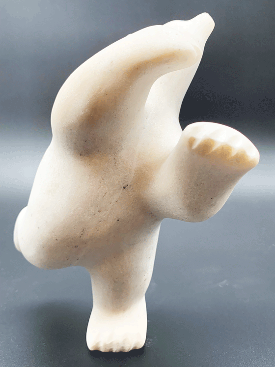 A dancing bear carved from white alabaster. This bear dances on one hind foot, with the other thrown back and arms spread wide. It throws its head back in jubilation. This bear faces the viewer.
