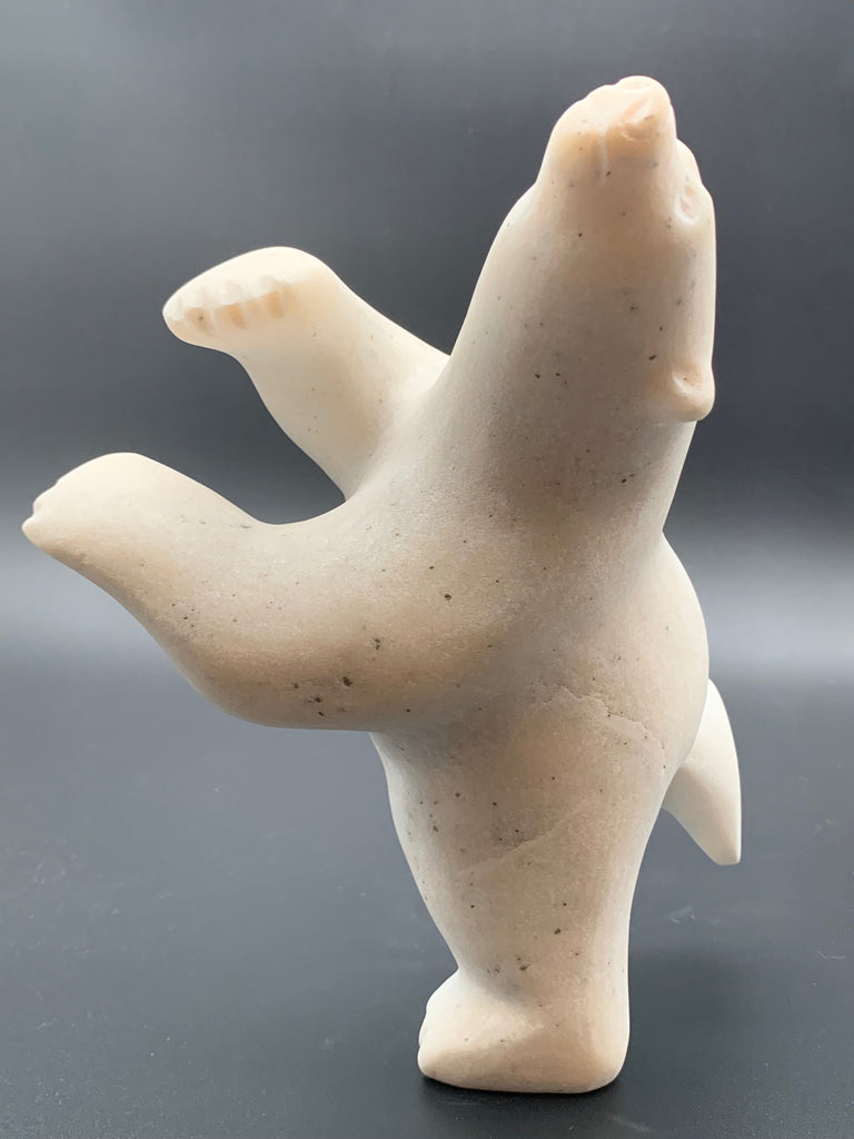 A dancing bear carved from white alabaster. This bear dances on one hind foot, with the other thrown back and arms spread wide. It throws its head back in jubilation. This bear faces left.