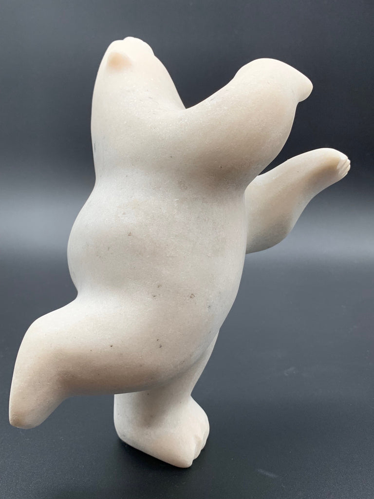 A dancing bear carved from white alabaster. This bear dances on one hind foot, with the other thrown back and arms spread wide. It throws its head back in jubilation. This bear faces right.