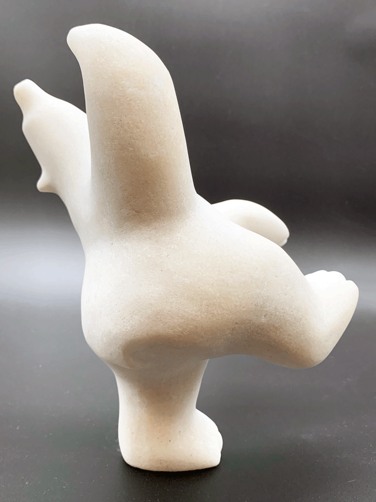 A dancing bear carved from white alabaster. This bear dances on one hind foot, with the other thrown in front of it and arms spread wide. It throws its head back in jubilation. This bear faces right.