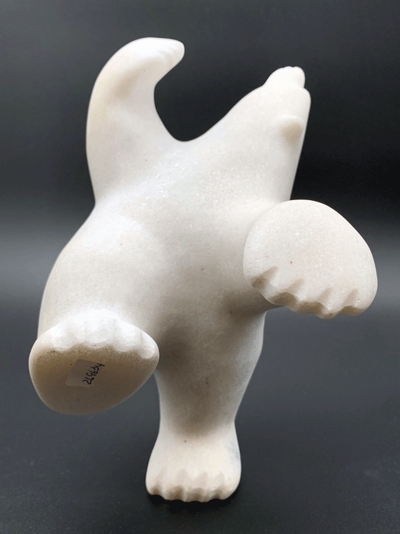 A dancing bear carved from white alabaster. This bear dances on one hind foot, with the other thrown in front of it and arms spread wide. It throws its head back in jubilation. This bear faces the viewer.