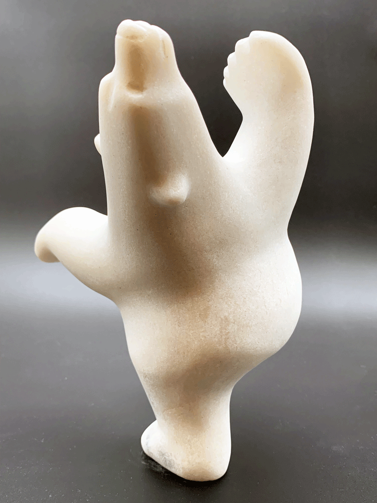 A dancing bear carved from white alabaster. This bear dances on one hind foot, with the other thrown in front of it and arms spread wide. It throws its head back in jubilation. This bear faces away.