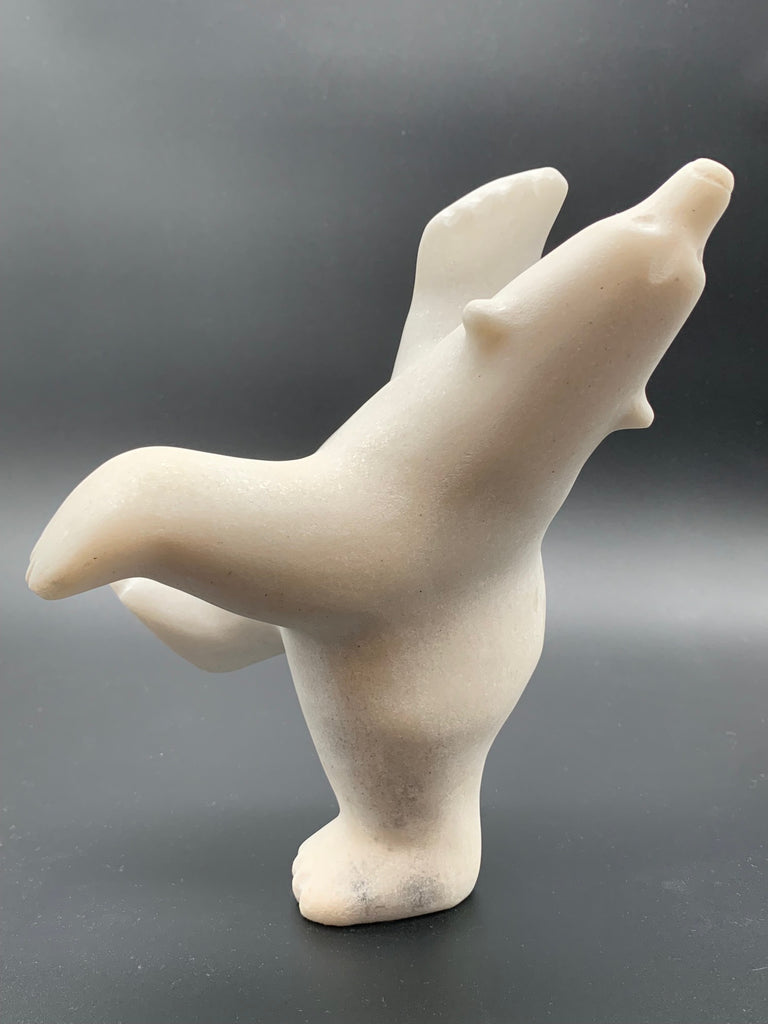 A dancing bear carved from white alabaster. This bear dances on one hind foot, with the other thrown in front of it and arms spread wide. It throws its head back in jubilation. This bear faces left.