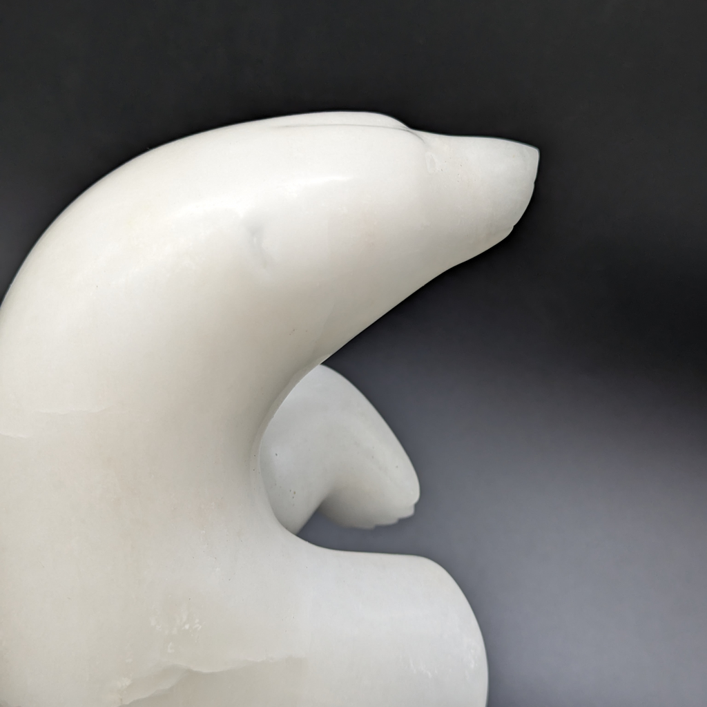 A close up of the dancing bear carved from white alabaster. The bear dances on one foot, with the other hind foot raised and its paws in front of it. This bear faces right.