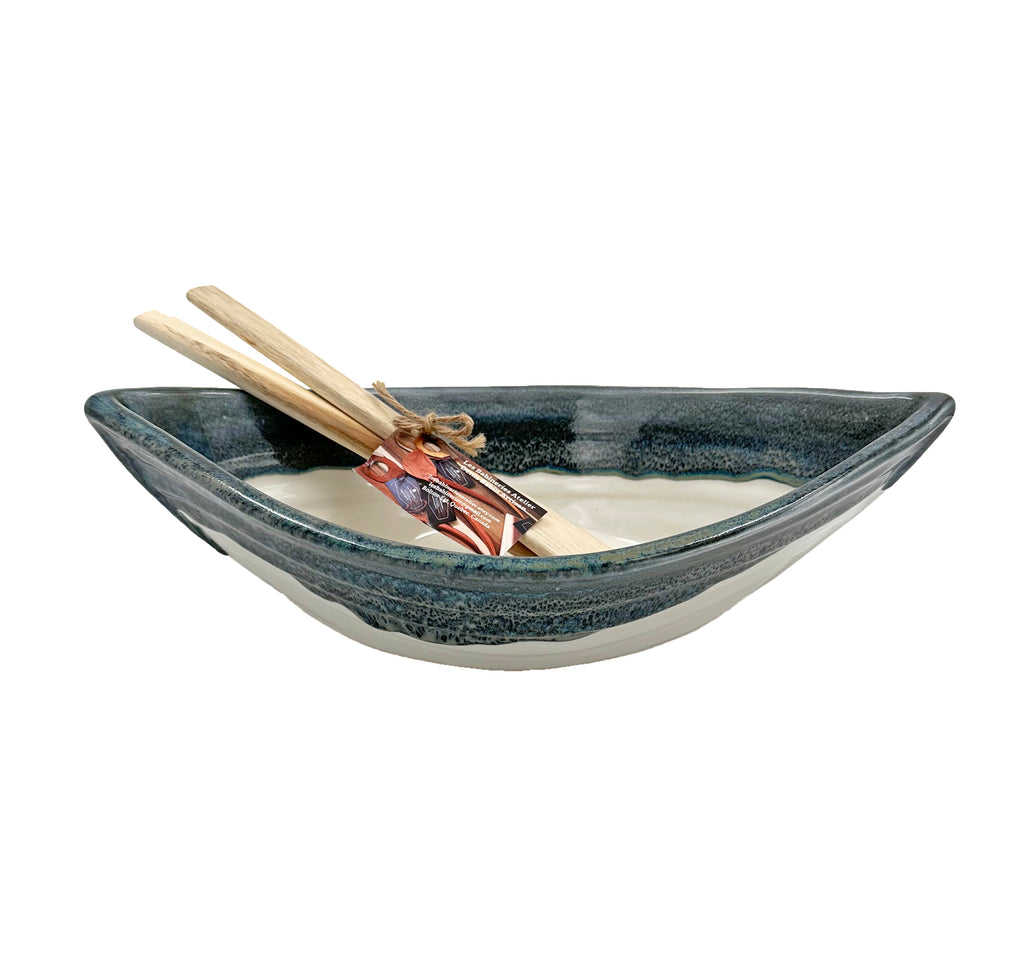 Bottom half of bowl is off-white. Top half of bowl is blue with white accents. Bowl is oval shaped with points at two opposite ends. Two wooden paddles sitting inside bowl.