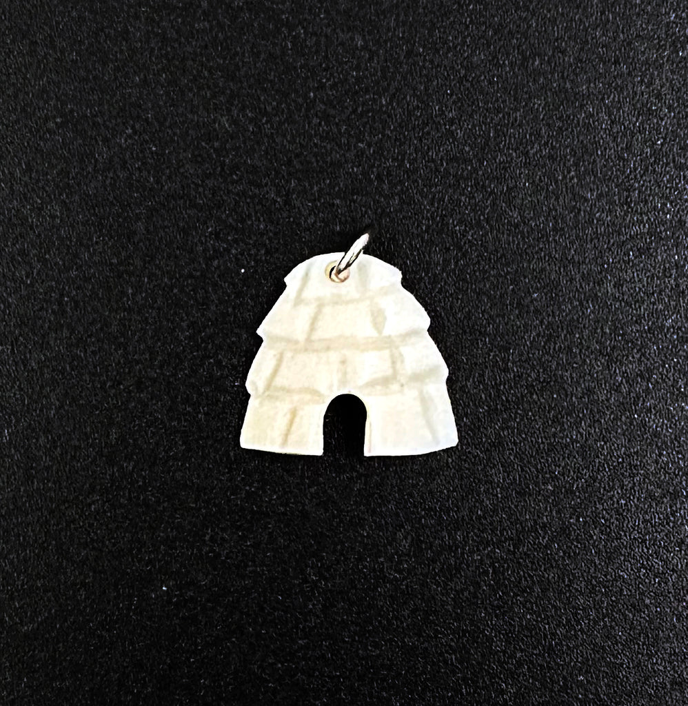 An off-white igloo pendant. The snowblocks are indented and create texture, and the entrance of the igloo is cut out. A small silver hook goes through a hole at the top of the igloo.