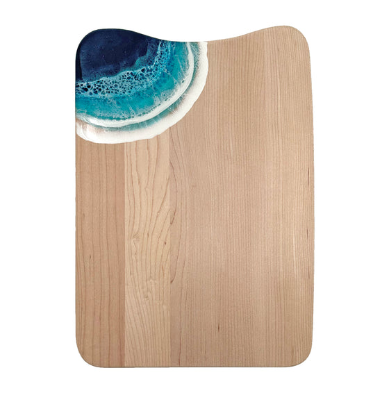 A large serving board made out of maple wood. In the corner are blue acrylic ocean waves.