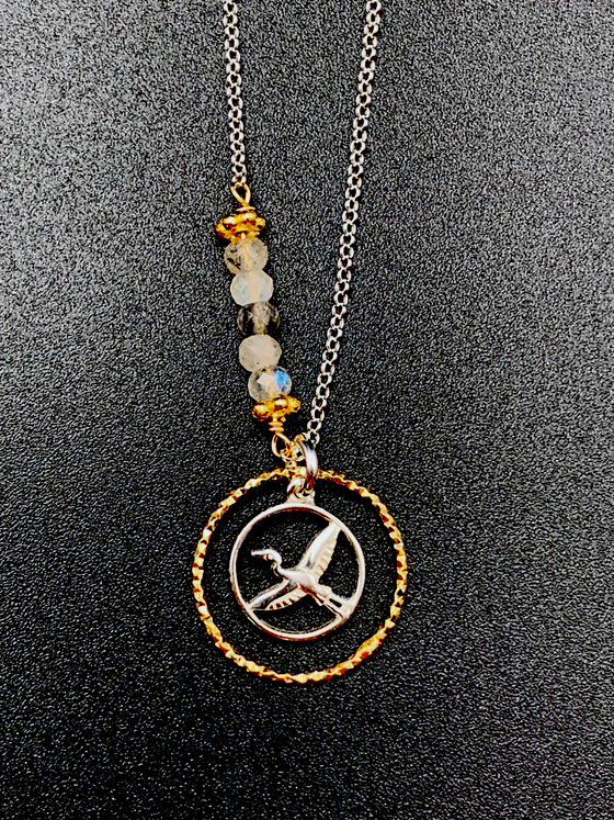 Silver chain with 5 coloured beads in middle of chain attached with gold chain links that look like flowers. Pendent is a gold ring that has triangle ridges. Small silver ring inside the gold one with a heron in the center. 