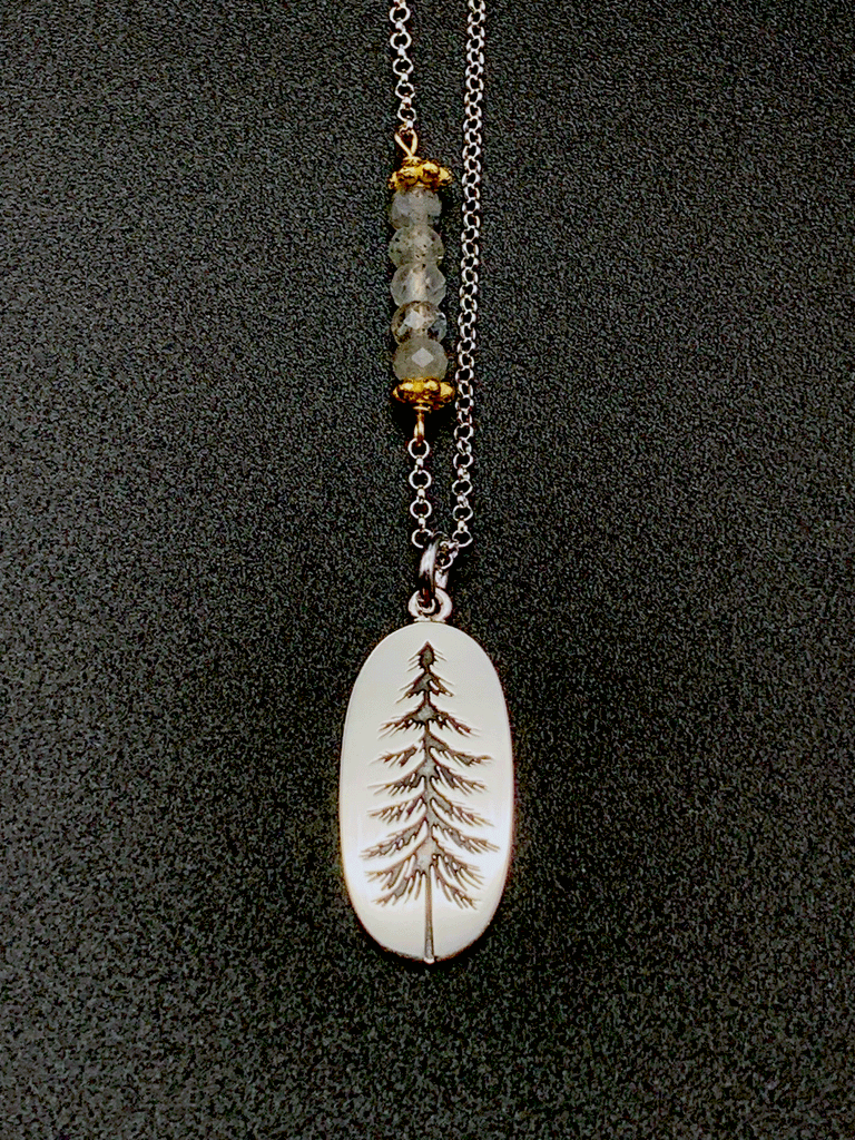 Silver chain with 5 coloured beads in middle of chain attached with gold chain links that look like flowers. Pendent is a silver oval with an indent of a pine tree. The indent of the pine tree is black. 