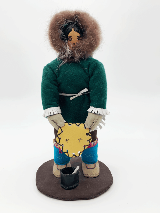 This handcrafted Inuit doll was created by Inuk artist Sophie Edmudluk in Puvurnituk, Nunavik and showcases a person in green traditional Inuit clothing standing over a pot