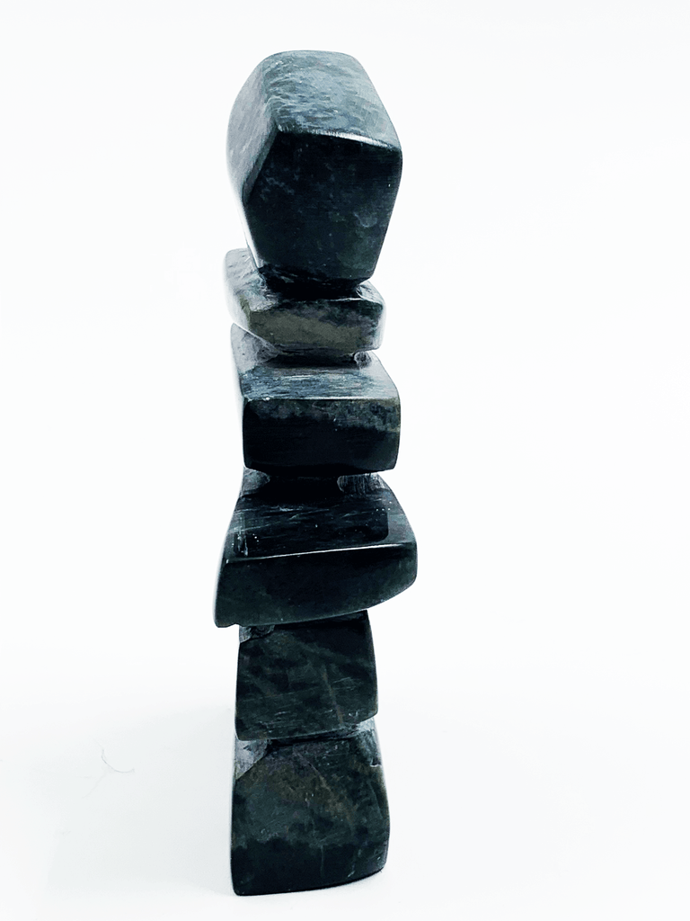 An inukshuk made of five slender slabs stacked on top of two broad legs and topped with a large head. The stone is vividly contrasting green and black. 