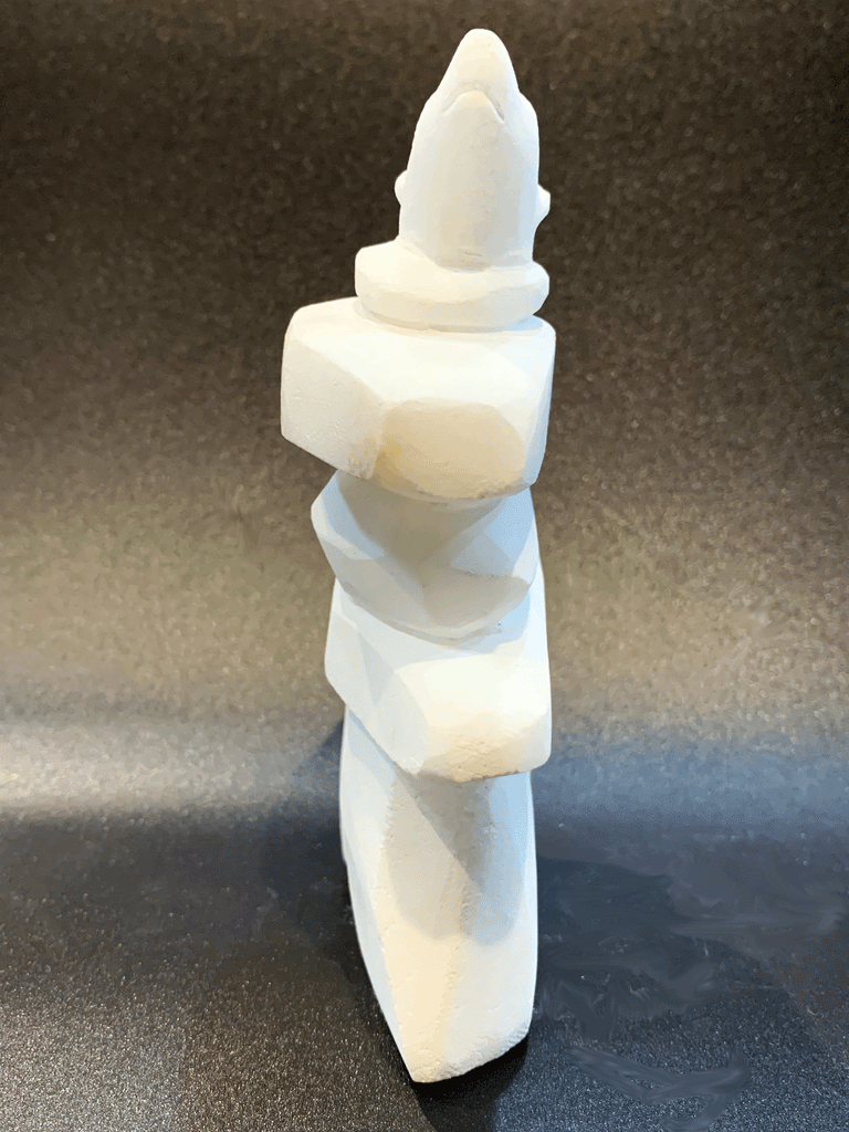 An inukshuk, the top stone of which is a polar bear head looking up, carved in one piece from white alabaster. The piece faces straight ahead in this image. The artist has used a special technique to etch fur texture into the bear and carving marks into the stone of the inukshuk for added realism.