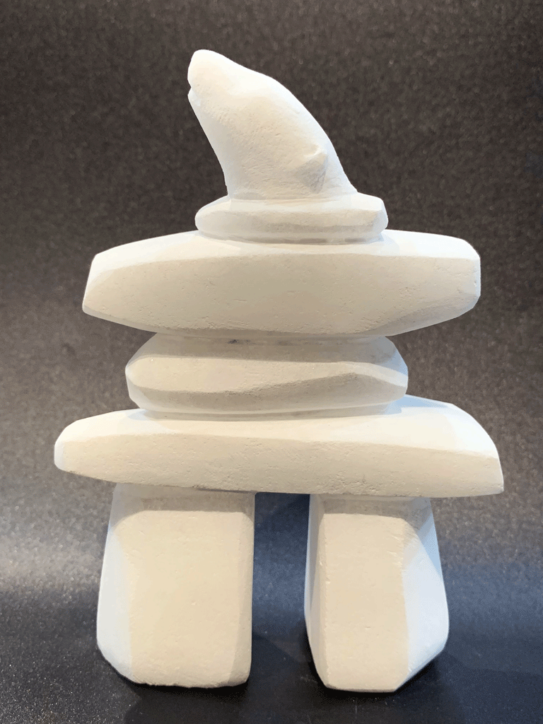An inukshuk, the top stone of which is a polar bear head looking up, carved in one piece from white alabaster. The piece faces left in this image. The artist has used a special technique to etch fur texture into the bear and carving marks into the stone of the inukshuk for added realism.