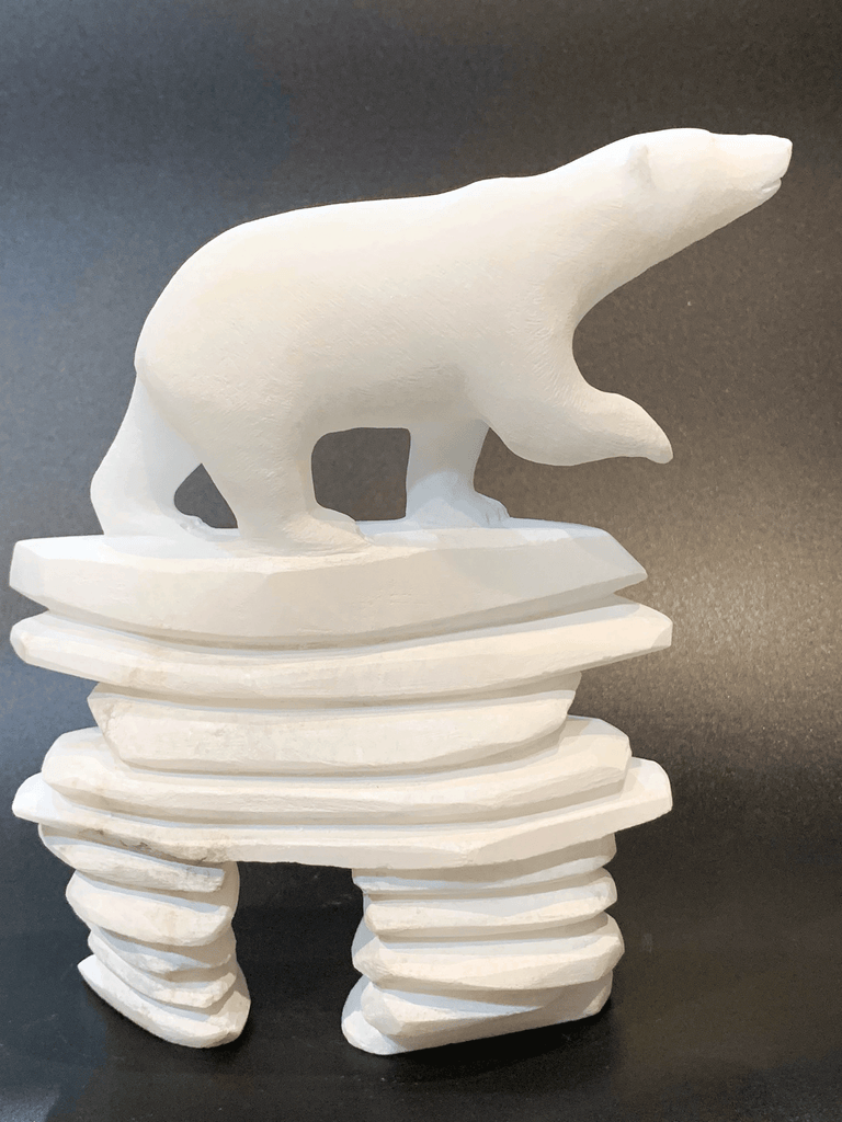A polar bear standing on top of an inukshuk base, carved in one piece from white alabaster. The polar bear faces right with one forepaw raised. The artist has used a special technique to etch fur texture into the bear and carving marks into the stone of the inukshuk for added realism.