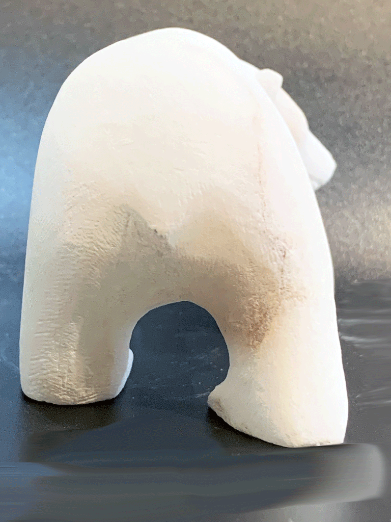 A polar bear carved from white alabaster stands on all fours. Its back is to the camera, head tilted to look at something to the right. The artist has used a special technique to etch fur texture into the bear for added realism.
