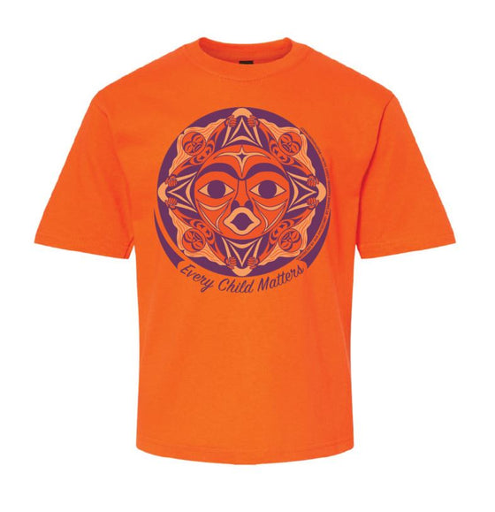 An orange shirt. In the middle there is an indigenous design resembling a face. The design is in the shape of a circle and underneath is written "Every Child Matters" in cursive font. The design and text is in purple and there are light orange details.