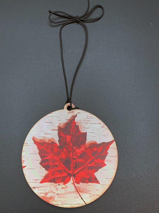 A flat, circular wooden ornament featuring a dimensional red maple leaf and a white wood-textured background.