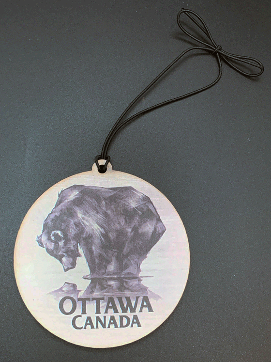 A flat, circular wooden ornament featuring a black bear staring down at its reflection against a white background. The words "Ottawa, Canada" are written in black beneath the bear.