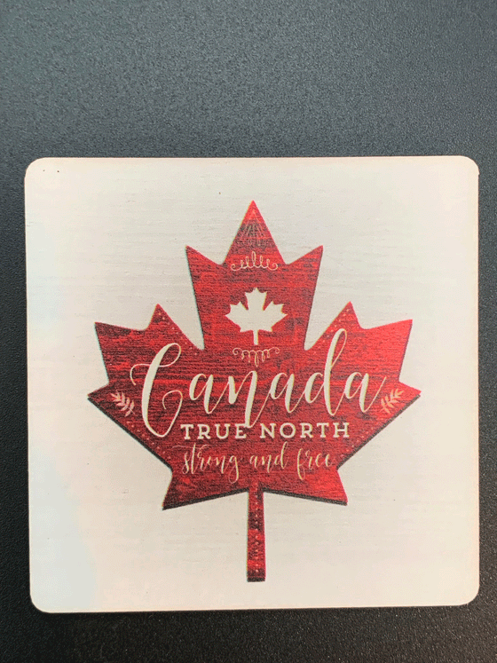 A square wooden magnet with rounded corners featuring a red maple leaf against a white background. White text written on the maple leaf reads "Canada True North Strong and Free".