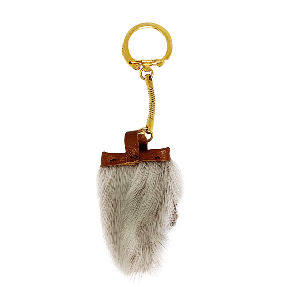 A small sealskin mitten keychain. The fur is grey and the top is a brown leather where a gold keychain is attached.