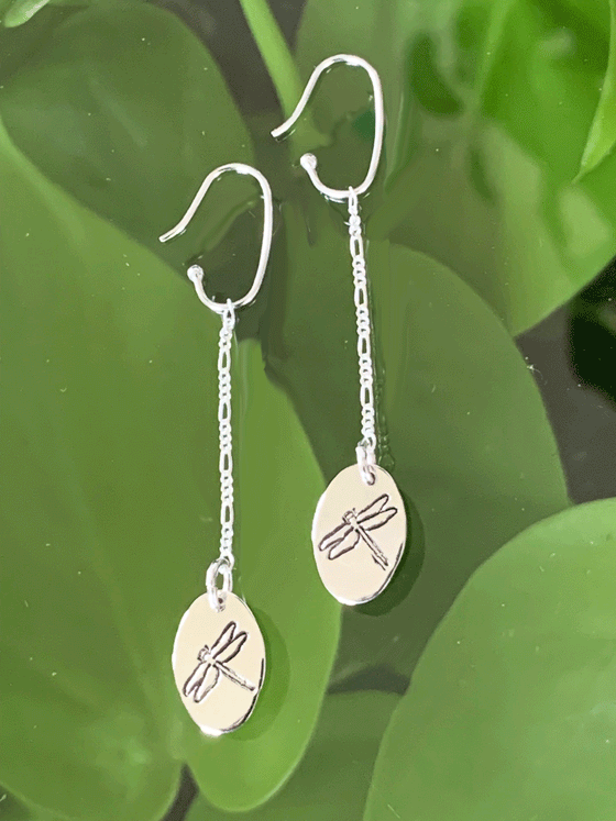 Drop earrings made of bright polished silver attached to sterling silver hooks.  The earrings are sterling ovals with a dragonfly etched in the centre.