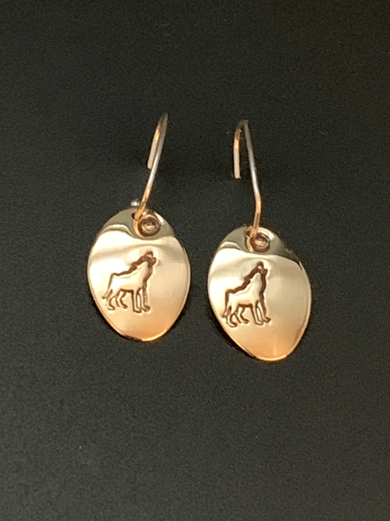 Drop earrings made of bright 14 karat gold fill and sterling silver attached to gold hooks.  The earrings are gold ovals with a wolf howling at the moon etched in the centre.