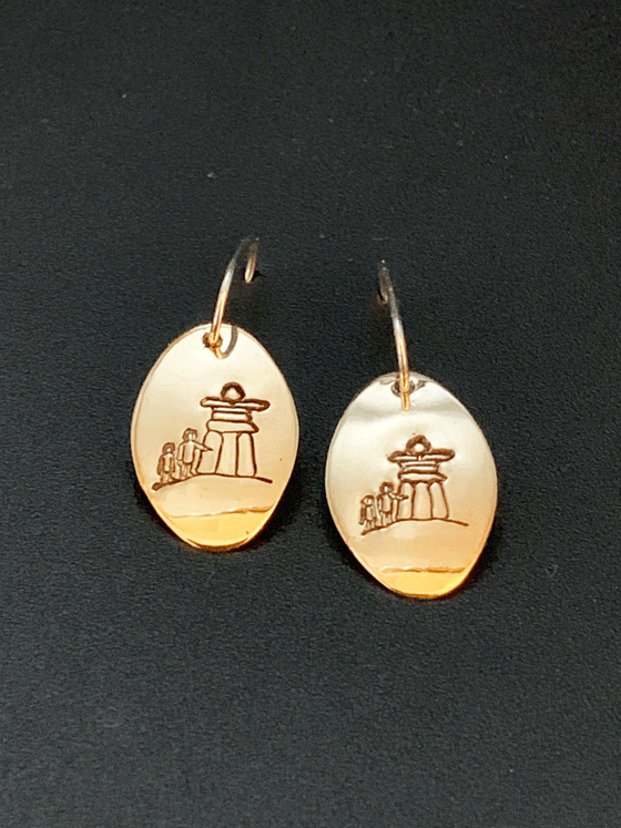 Drop earrings made of bright 14 karat gold fill and sterling silver attached to gold hooks.  The earrings are gold ovals with a large inukshuk with two smaller human figures  etched in the centre.