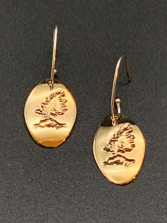 Drop earrings made of bright 14 karat gold fill and sterling silver attached to gold hooks.  The earrings are gold ovals with a rugged windswept pine on rock etched in the centre.
