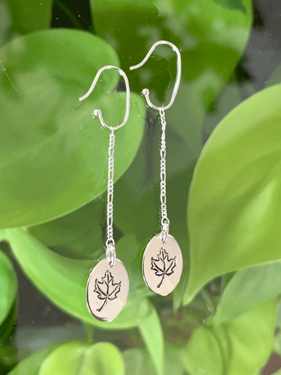 Drop earrings made of bright polished silver attached to sterling silver hooks.  The earrings are sterling ovals with a maple leaf etched in the centre.