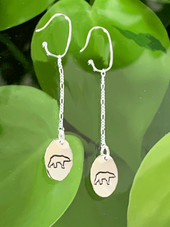 Drop earrings made of bright polished silver attached to sterling silver hooks.  The earrings are sterling ovals with a polar bear etched in the centre.