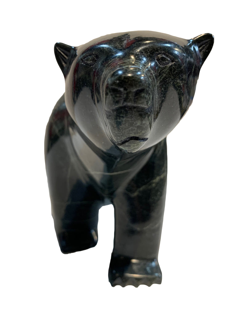 A large bear carved from dark green - almost black - stone. The bear walks on all fours, with its left hind leg slightly raised. The artist has carved powerful haunches and neck, conveying incredible power and strength in the animal. This bear faces the viewer, pushing its snout right into the camera.
