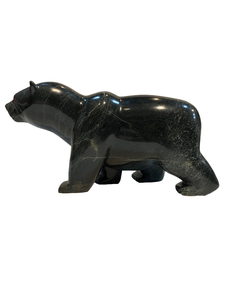 A large bear carved from dark green - almost black - stone. The bear walks on all fours, with its left hind leg slightly raised. The artist has carved powerful haunches and neck, conveying incredible power and strength in the animal. This bear faces left.
