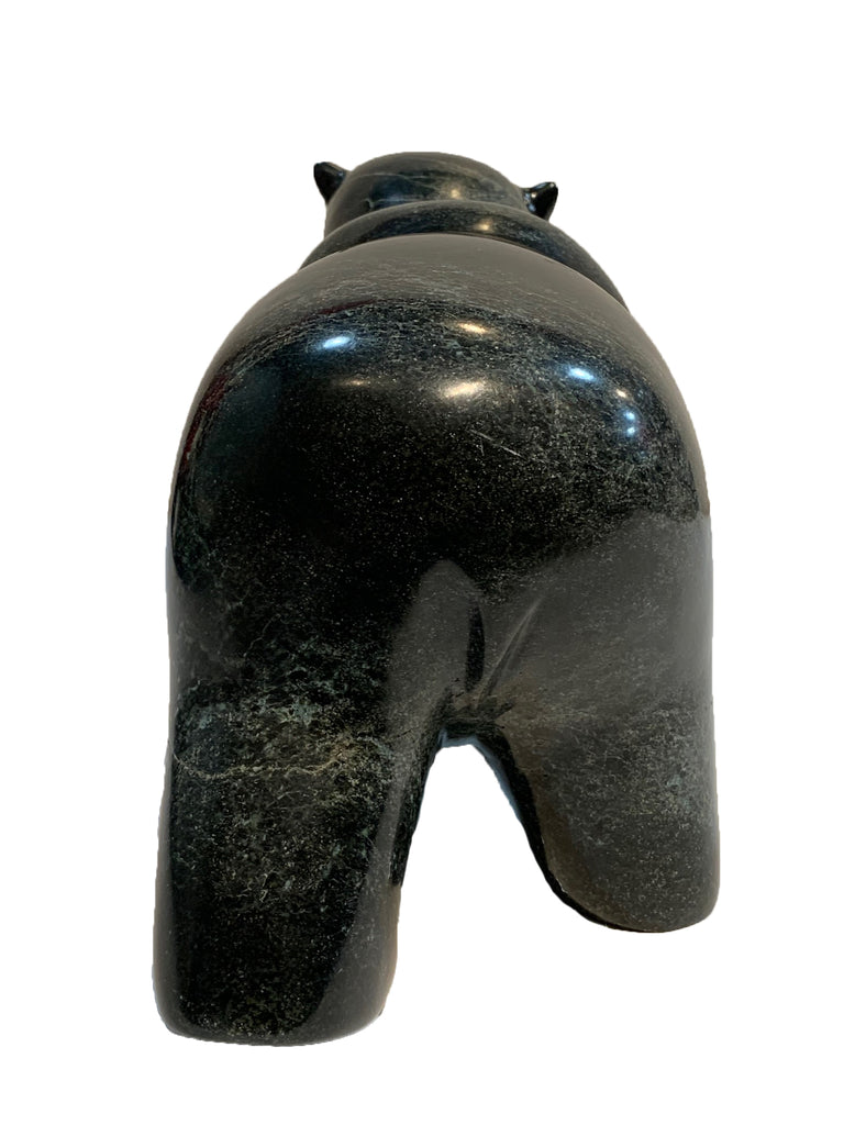 A large bear carved from dark green - almost black - stone. The bear walks on all fours, with its left hind leg slightly raised. The artist has carved powerful haunches and neck, conveying incredible power and strength in the animal. This bear faces away.
