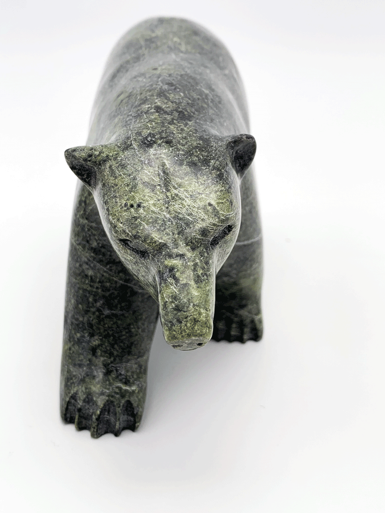 A closeup of a green soapstone bear walking on all fours. The extreme closeup showcases the subtle details and expression the artist has brought to the bear's face and paws.