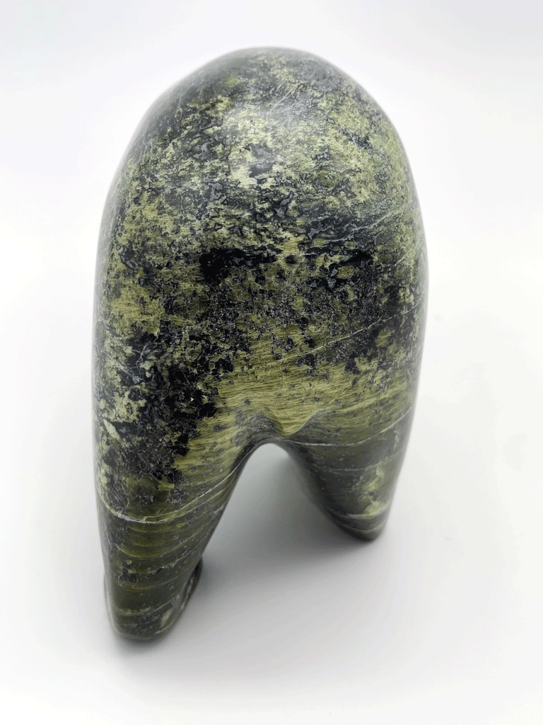 A bear carved of green soapstone stands on all fours. This bear faces away, showing off the beautiful mottling and striations in the stone.