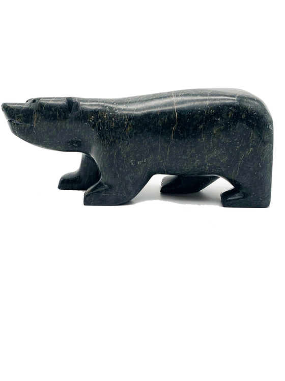 A smiling walking bear carved from very dark green soapstone stands on all fours. Its head is cocked playfully to one side. This bear faces left.