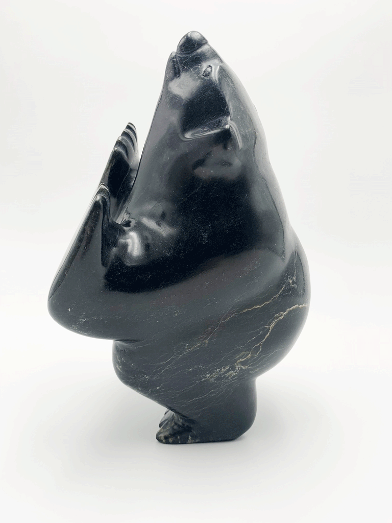 A dancing bear carved from very dark green - nearly black - stone. This bear dances on one hind foot, with the other raised to one side and front paws raised. Its head is thrown back in jubilation. This bear faces left.
