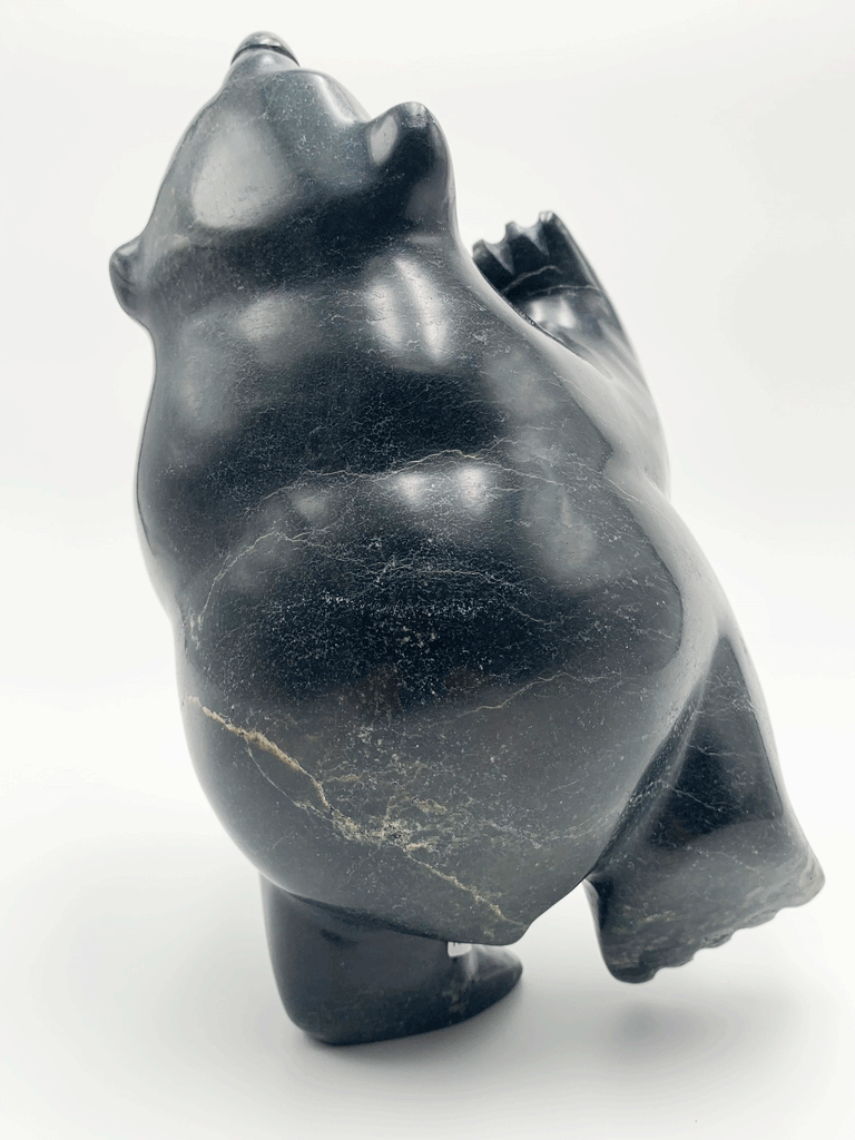 A dancing bear carved from very dark green - nearly black - stone. This bear dances on one hind foot, with the other raised to one side and front paws raised. Its head is thrown back in jubilation. This bear faces away.