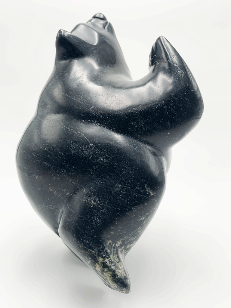 A dancing bear carved from very dark green - nearly black - stone. This bear dances on one hind foot, with the other raised to one side and front paws raised. Its head is thrown back in jubilation. This bear faces right.