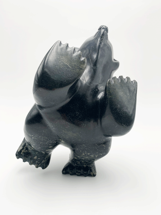 A dancing bear carved from very dark green - nearly black - stone. This bear dances on one hind foot, with the other raised to one side and front paws raised. Its head is thrown back in jubilation. This bear faces the viewer.