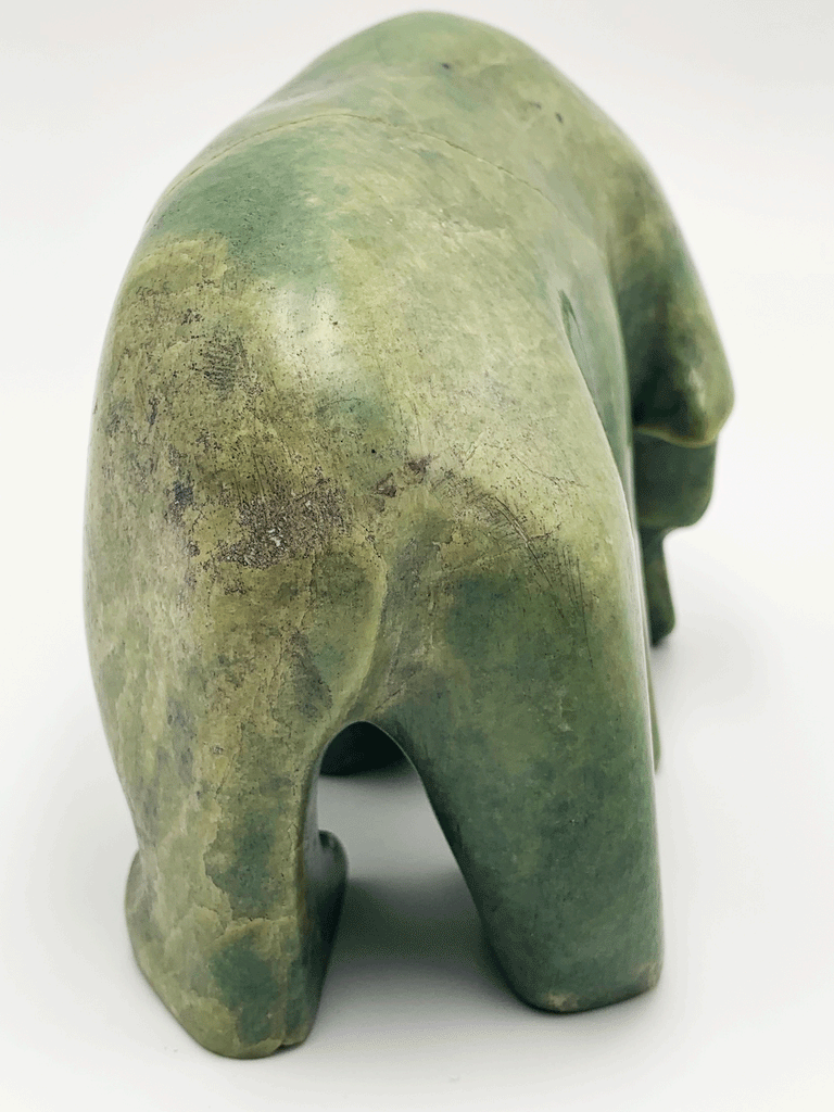 An inquisitive, bright green soapstone bear stands on all fours, head bowed as though examining something on the ground. This bear faces away.