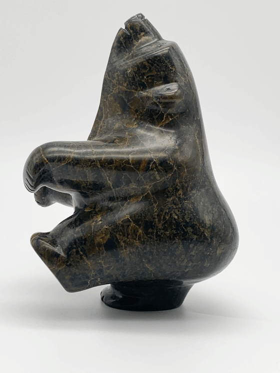 A dancing bear carved from greenish brown stone. This bear dances on one hind foot, with the other raised to one side and front paws raised. It throws its head back in jubilation. This bear faces left.