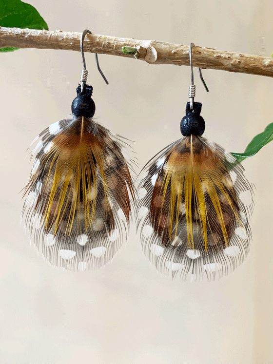 Dangling earrings featuring a brown and black feather with yellow streaks and white spots hanging on a silver-coloured stainless steel hook.