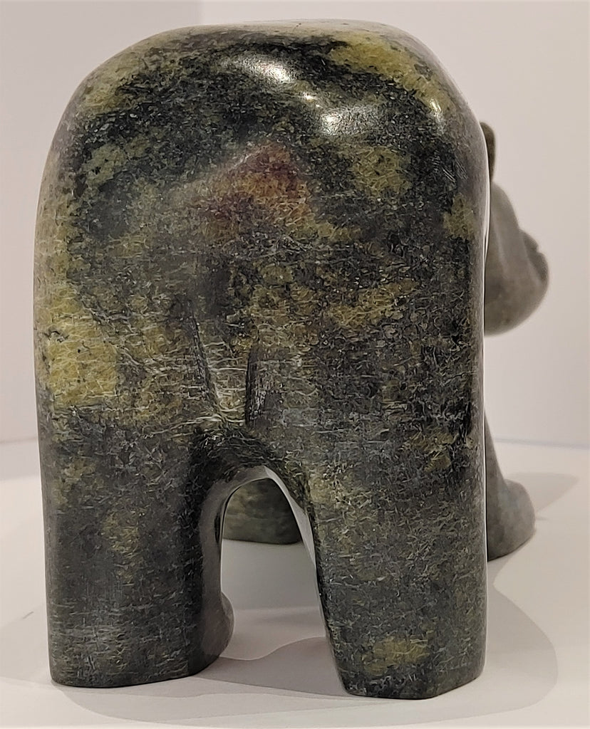 A closeup of an attentive bear standing on all fours, carved from mottled green soapstone. This bear faces away.