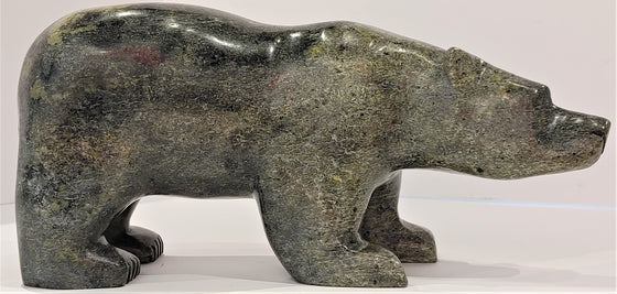 A closeup of an attentive bear standing on all fours, carved from mottled green soapstone. This bear faces right.
