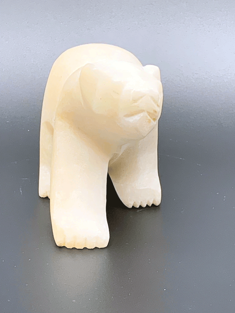 A white polar bear carved from alabaster walks on all fours. This bear faces the viewer.