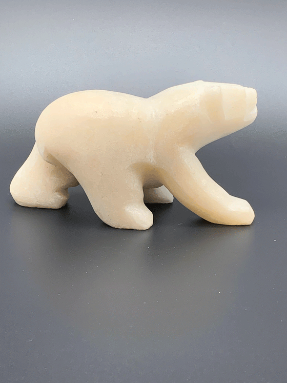 A white polar bear carved from alabaster walks on all fours. This bear faces right.