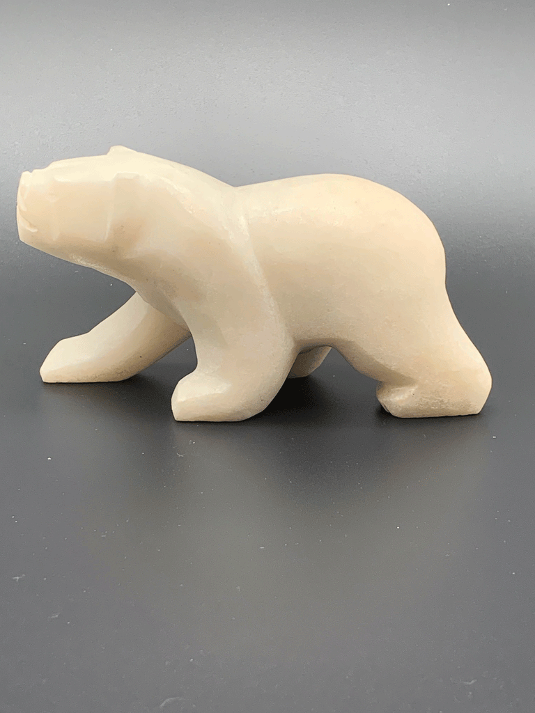 A white polar bear carved from alabaster walks on all fours. This bear faces left.